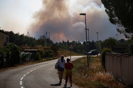 Des personnes marchent le long d’une route tandis qu’un épais nuage de fumée s’élève à l’arrière-plan à Carcassonne, dans le département de l’Aude, dans un contexte de sécheresse aggravée après une vague de chaleur et des pénuries d’eau dans une grande partie de la France, le 2 août 2026.